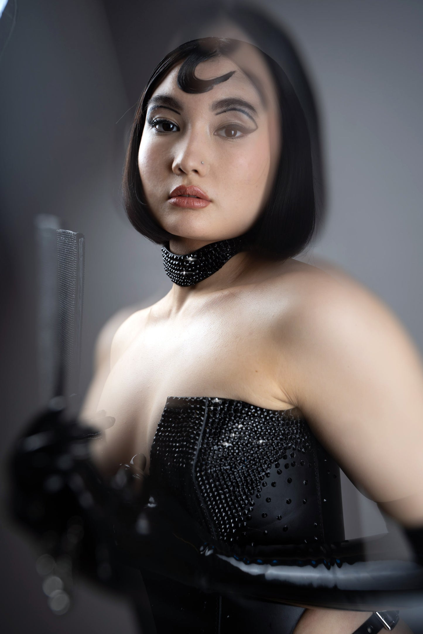 Woman wearing a black leather outfit with a high collar and gloves, holding a paddle.