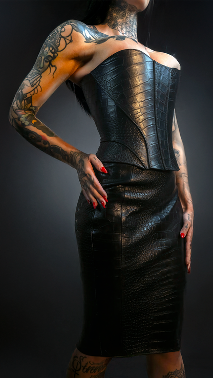 Person wearing a black leather outfit with tattoos on arms and back against a dark background