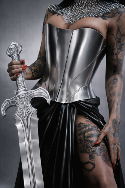 Person wearing a metallic corset and holding a sword against a gray background